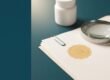 Leere Produktetiketten, Lineal und Lupe auf einem Arbeitstisch, daneben eine weiße Dose